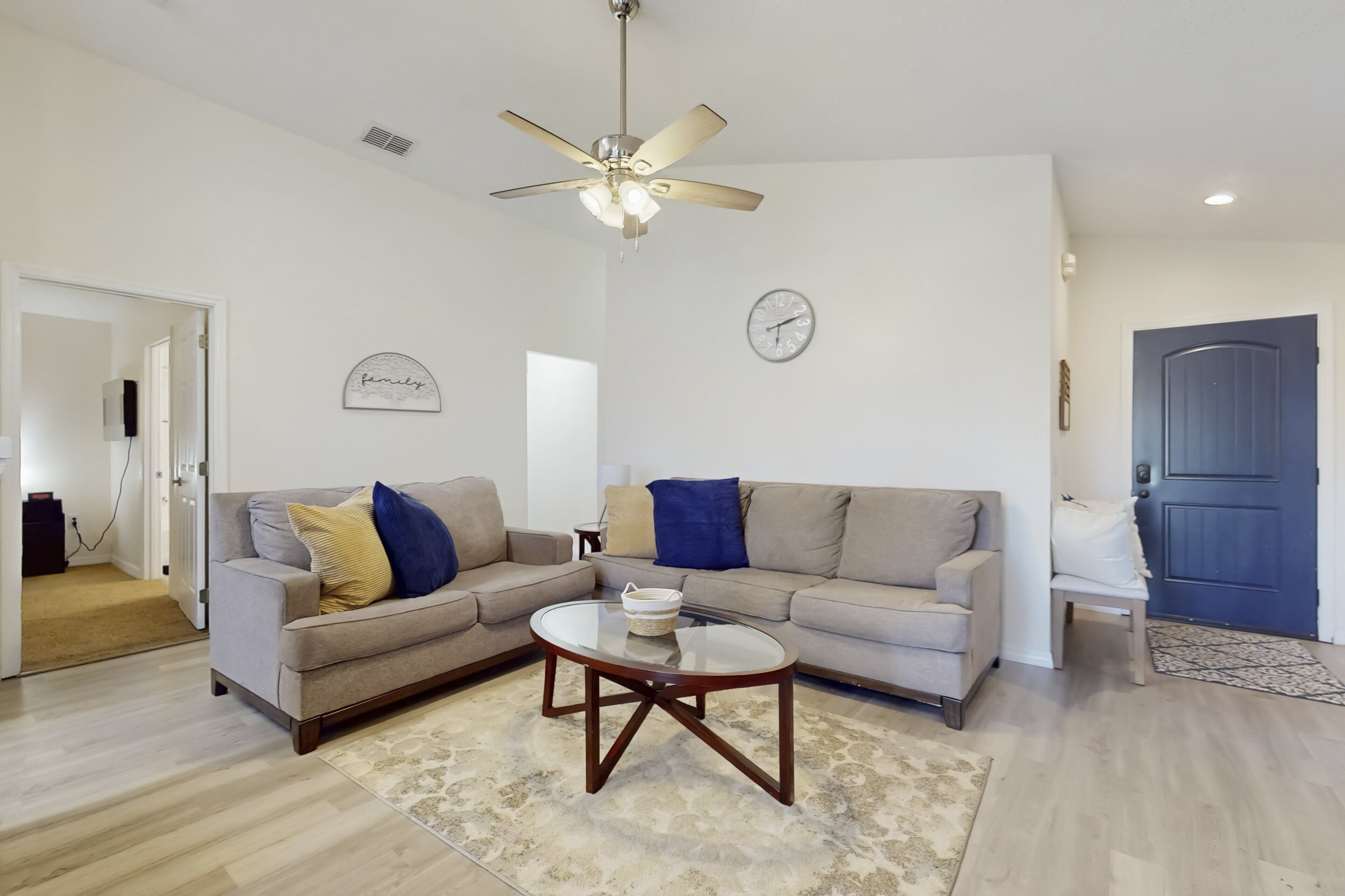A living room with a ceiling fan, two couches, a coffee table, and a clock on the wall.