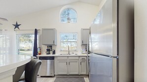 A modern kitchen with a built-in dishwasher, a stainless steel refrigerator, and a window with a view of trees. - Radiant Retreat With Private Pool, On-site Golf, Board Games, AC, & W/D (Haines City)