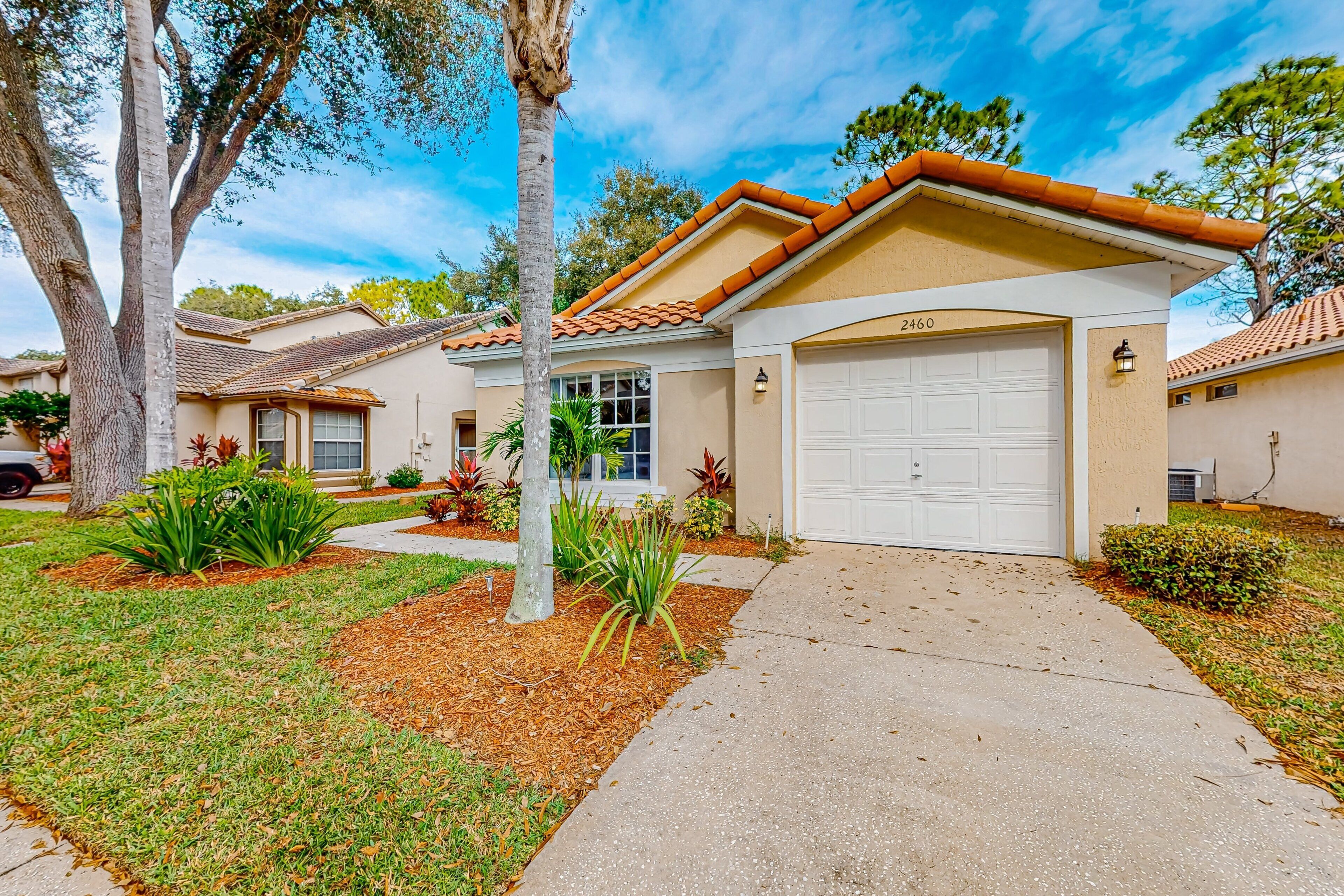 A residential house with a garage, a driveway, and a well-maintained lawn with various plants.