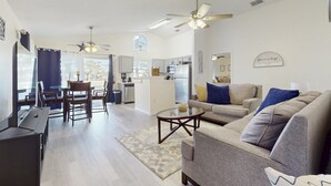 A modern living room with a sofa, coffee table, and dining area. - Radiant Retreat With Private Pool, On-site Golf, Board Games, AC, & W/D (Haines City)