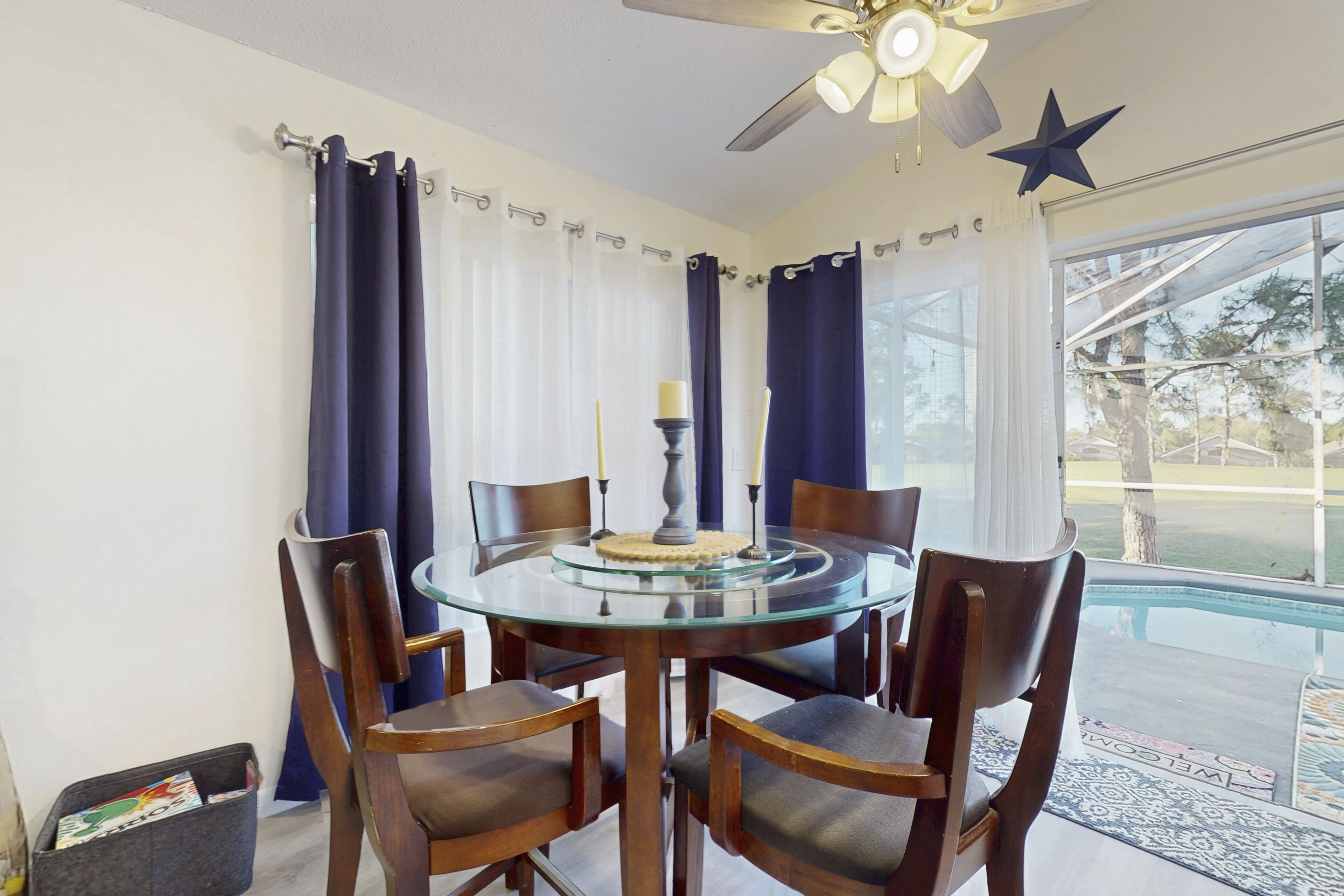 A round glass table with six wooden chairs, a ceiling fan, and a star decoration on the wall.