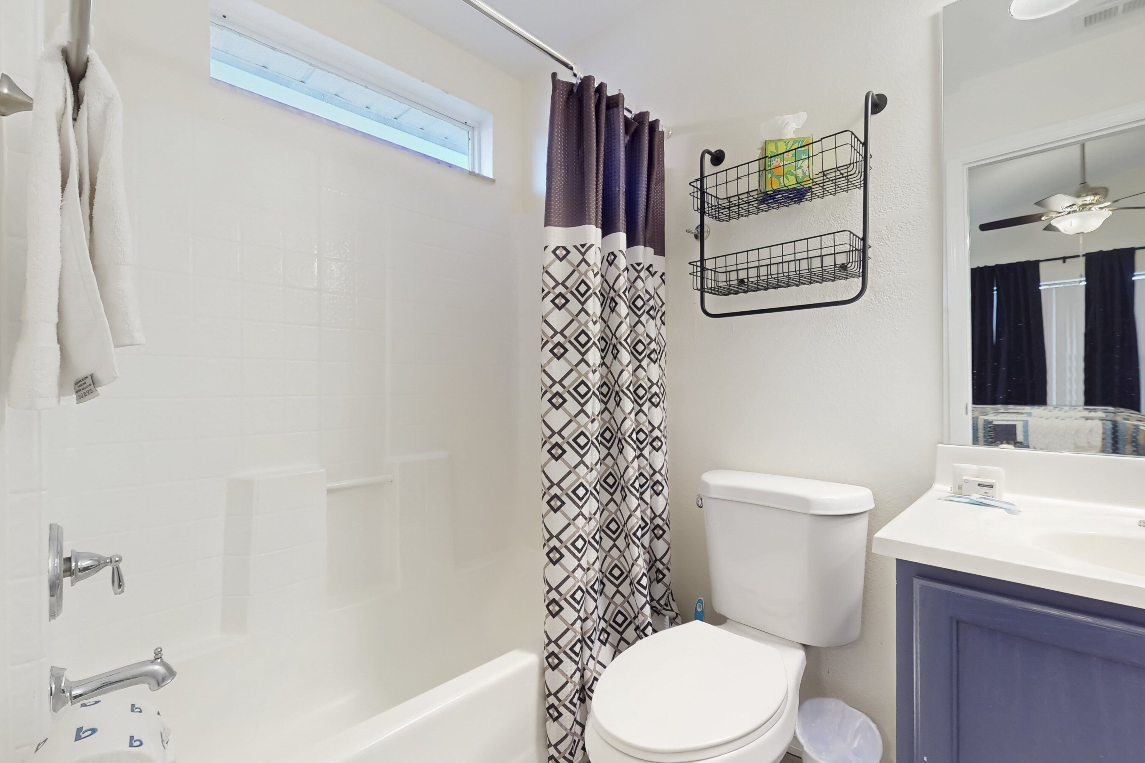 Une salle de bain avec une baignoire blanche, des toilettes, un rideau de douche à motifs géométriques et un porte-serviettes avec une serviette blanche.
