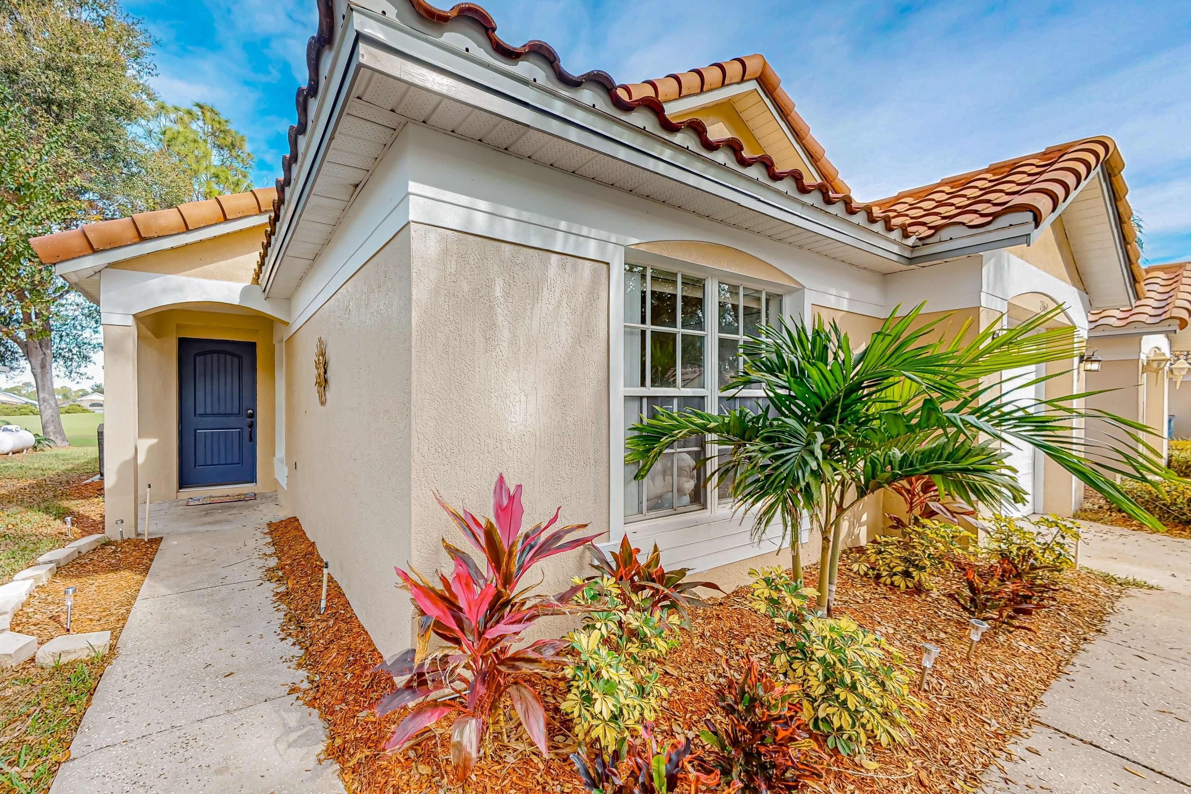A residential house with a beige exterior, a blue door, and a tiled roof.