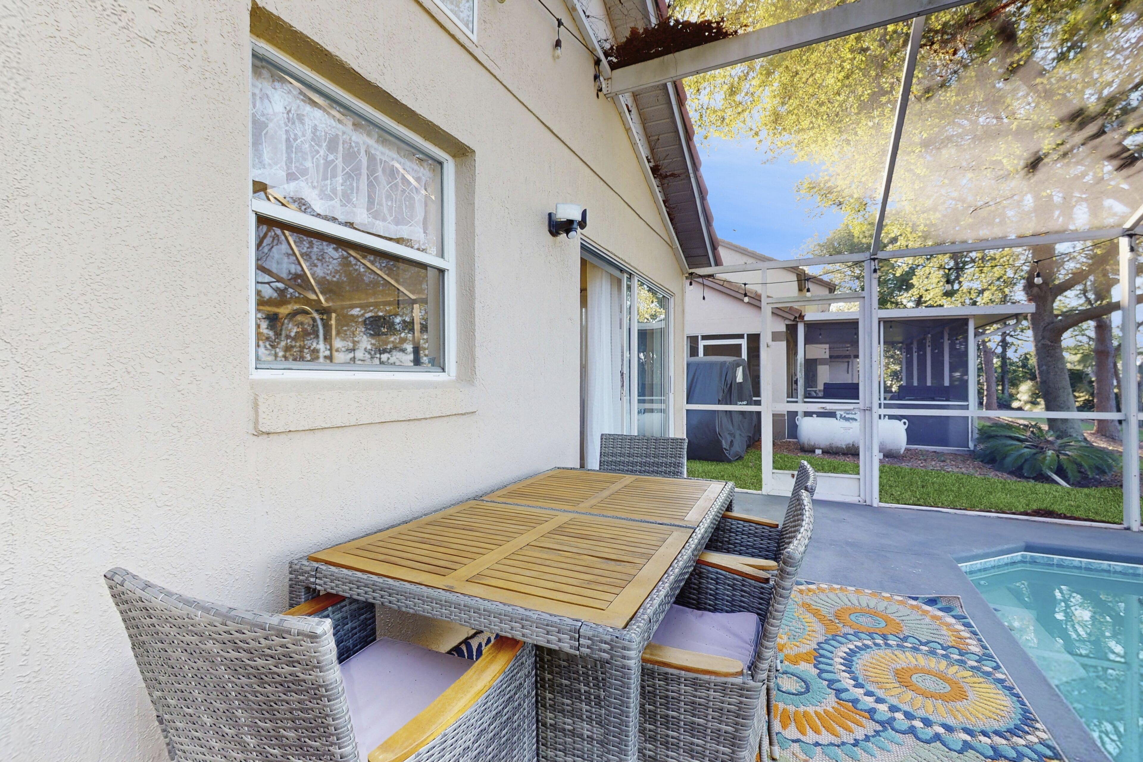 A covered patio with a pool, wicker furniture, and a patterned rug.