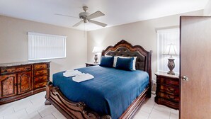 Een slaapkamer met een bed, een plafondventilator, een dressoir en een nachtkastje met een lamp.
