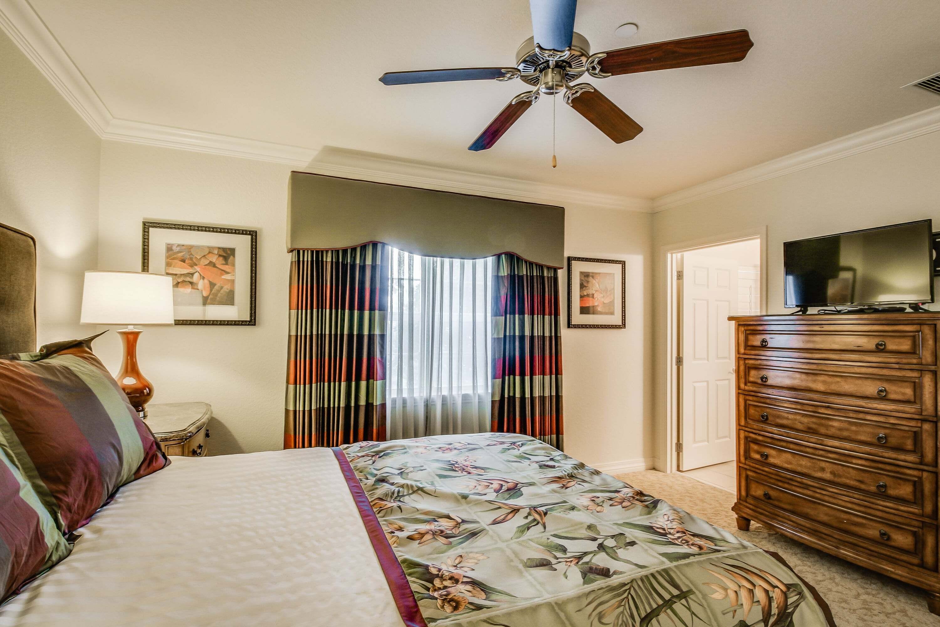 A bedroom with a bed, a dresser, a ceiling fan, and a television.