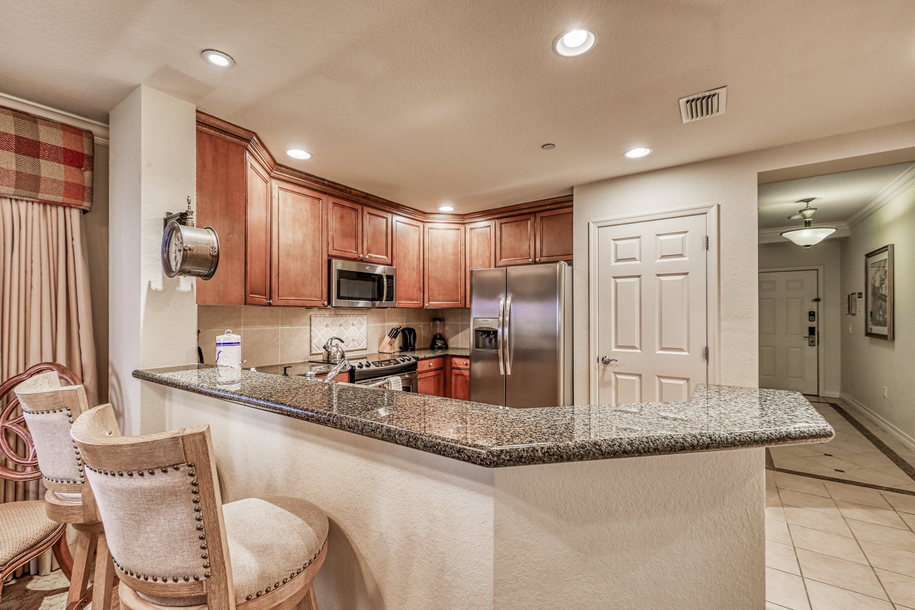 A kitchen with wooden cabinets, a granite countertop, a stainless steel refrigerator, and a built-in microwave.