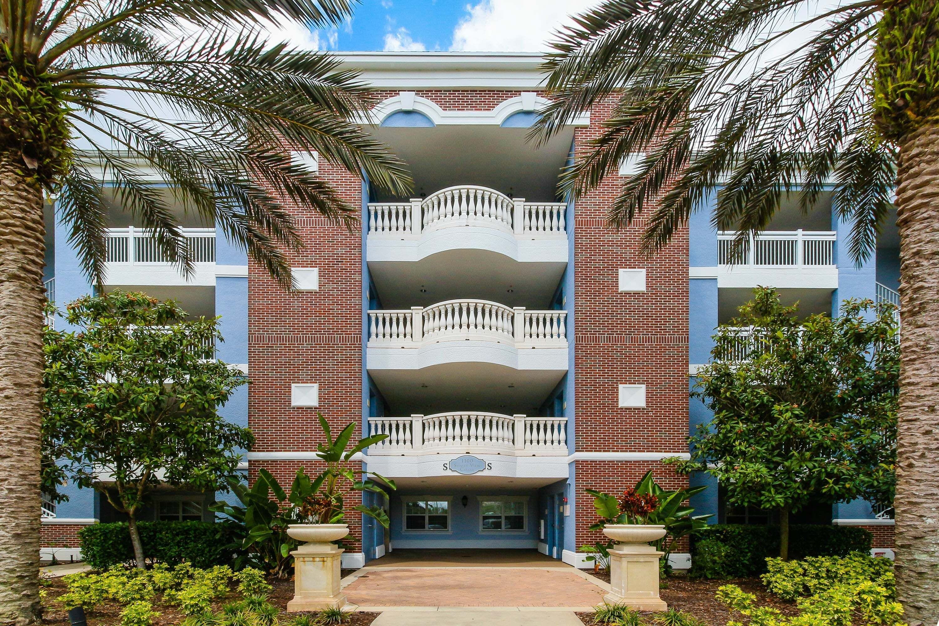 A multi-story building with a central entrance, surrounded by palm trees and a well-maintained garden.