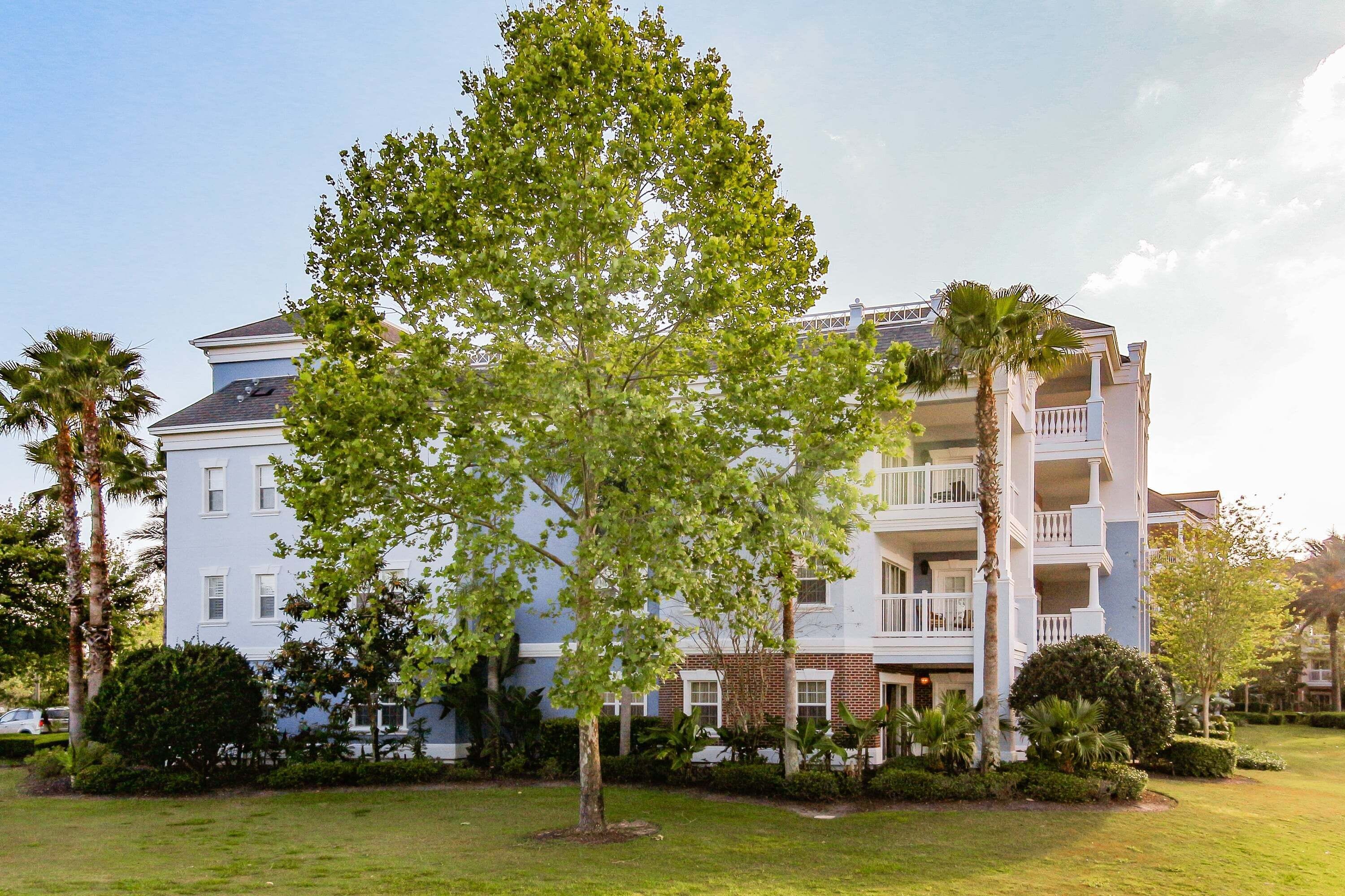 A multi-story hotel with a balcony on the second floor, surrounded by well-maintained lawns and trees.
