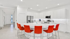A modern kitchen with white cabinetry, a central island with bar stools, stainless steel appliances, and recessed ceiling lighting. - Dog-friendly Home With a Heated Pool, Pool Spa, In-home Theater, Lanai, & Patio (Kissimmee)
