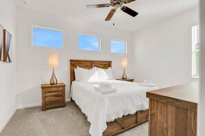 A bedroom with a wooden bed, two bedside tables, a ceiling fan, and three windows. - Dog-friendly Home With a Heated Pool, Pool Spa, In-home Theater, Lanai, & Patio (Kissimmee)