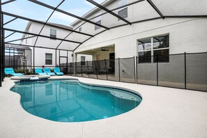 A swimming pool with blue tiles, a covered area with a ceiling, and a building with windows and a door. - Dog-friendly Home With a Heated Pool, Pool Spa, In-home Theater, Lanai, & Patio (Kissimmee)