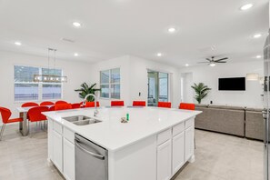 Uma cozinha moderna com ilha central, armários brancos e cadeiras vermelhas.