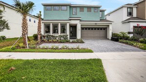 A two-story residential house with a garage, a front lawn, and palm trees. - Dog-friendly Home With a Heated Pool, Pool Spa, In-home Theater, Lanai, & Patio (Kissimmee)