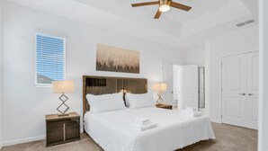 A bedroom with a bed, two bedside tables, a ceiling fan, a window with blinds, and a door. - Dog-friendly Home With a Heated Pool, Pool Spa, In-home Theater, Lanai, & Patio (Kissimmee)