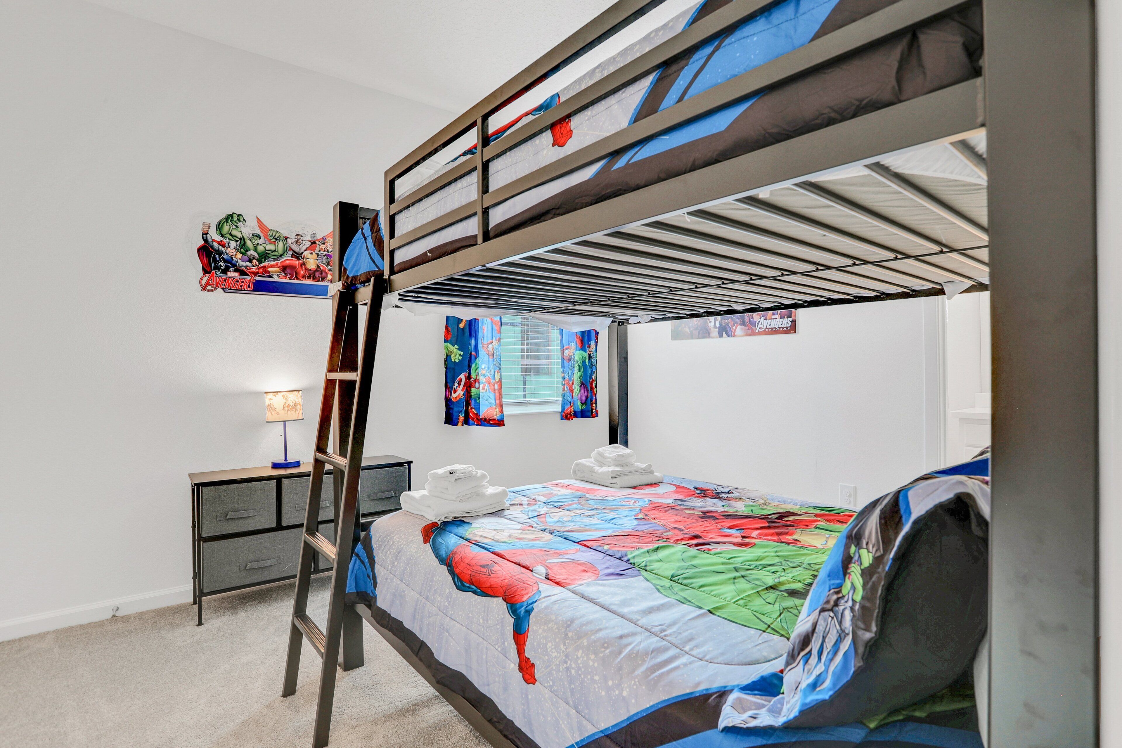 Un lit superposé avec une couverture aux couleurs vives, un bureau avec une lampe et une fenêtre avec des rideaux.