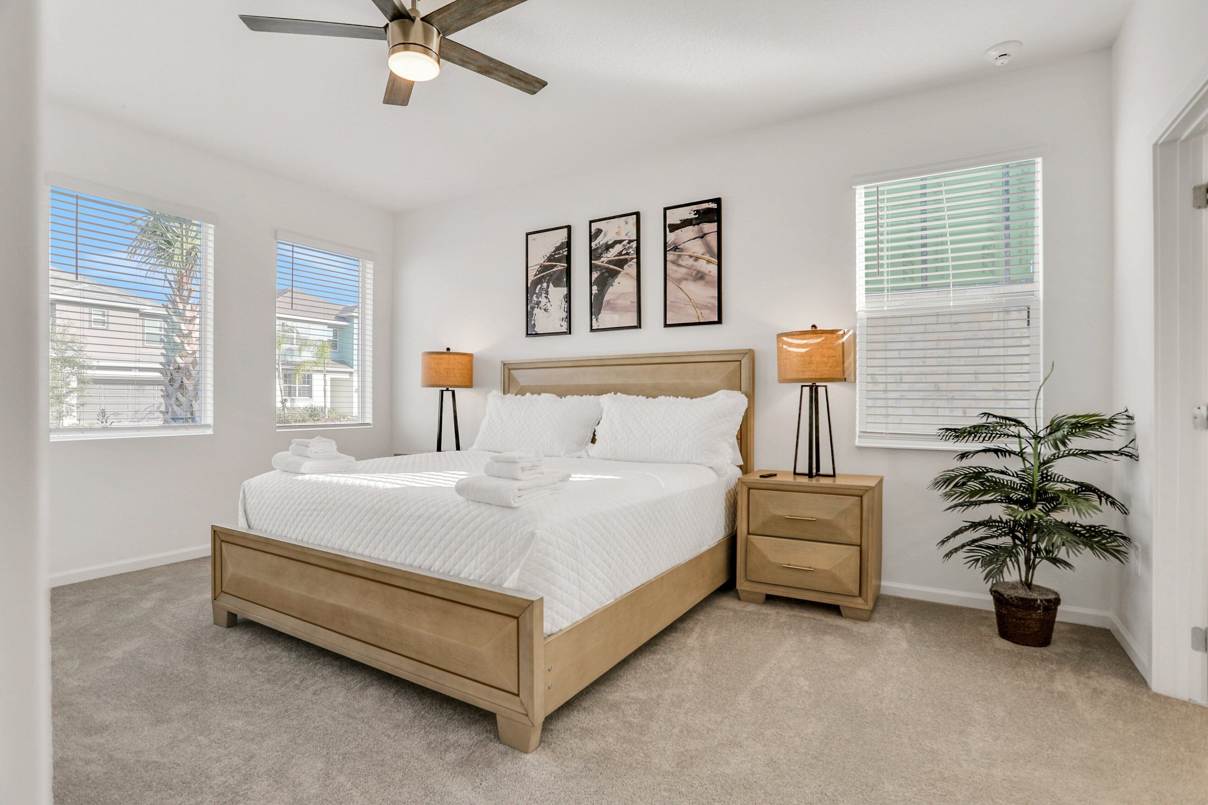 A bedroom with a bed, bedside tables, a ceiling fan, a potted plant, and artwork on the wall.