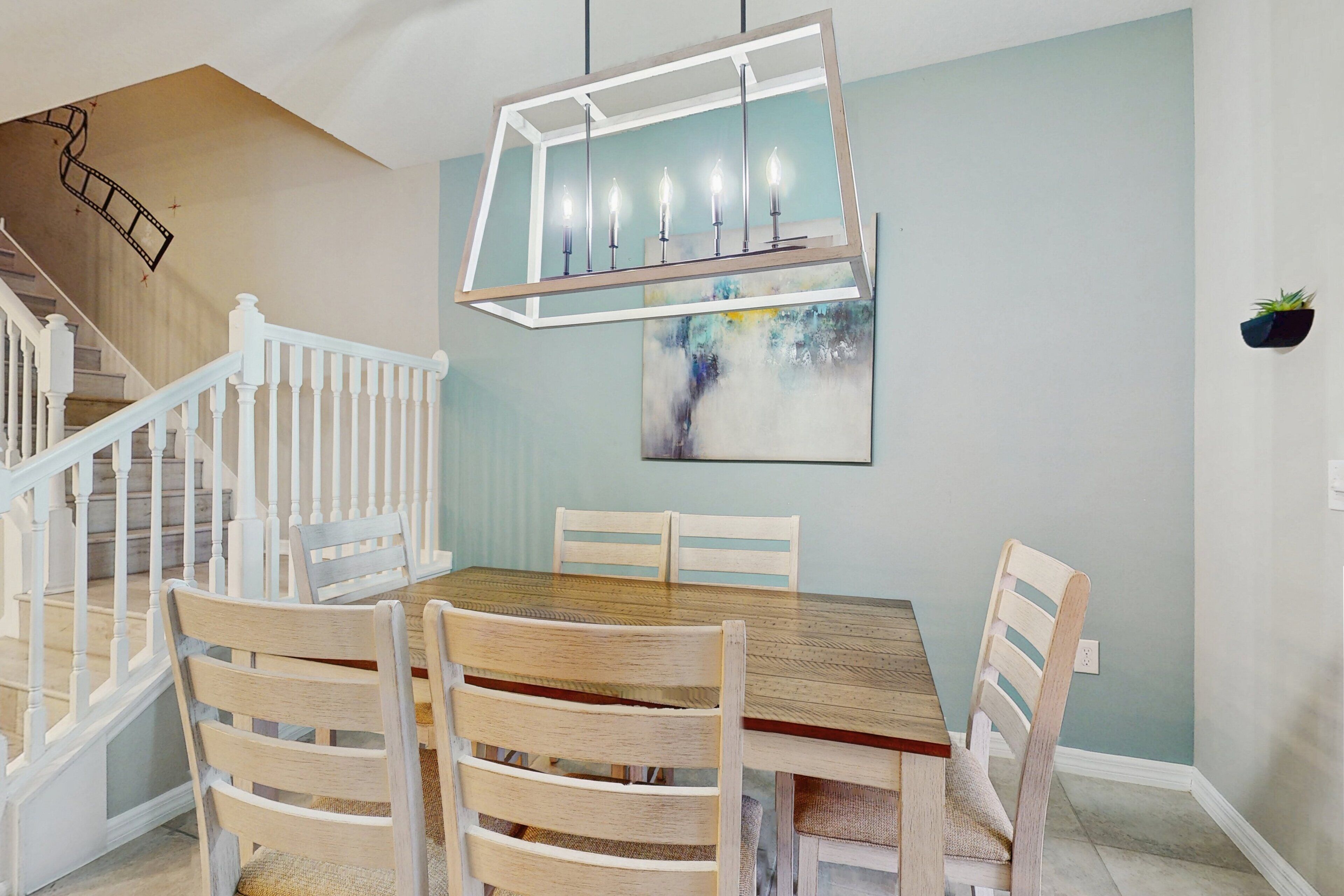 Een eetgedeelte met een houten tafel en stoelen, een trap met witte leuningen en een schilderij aan de muur.