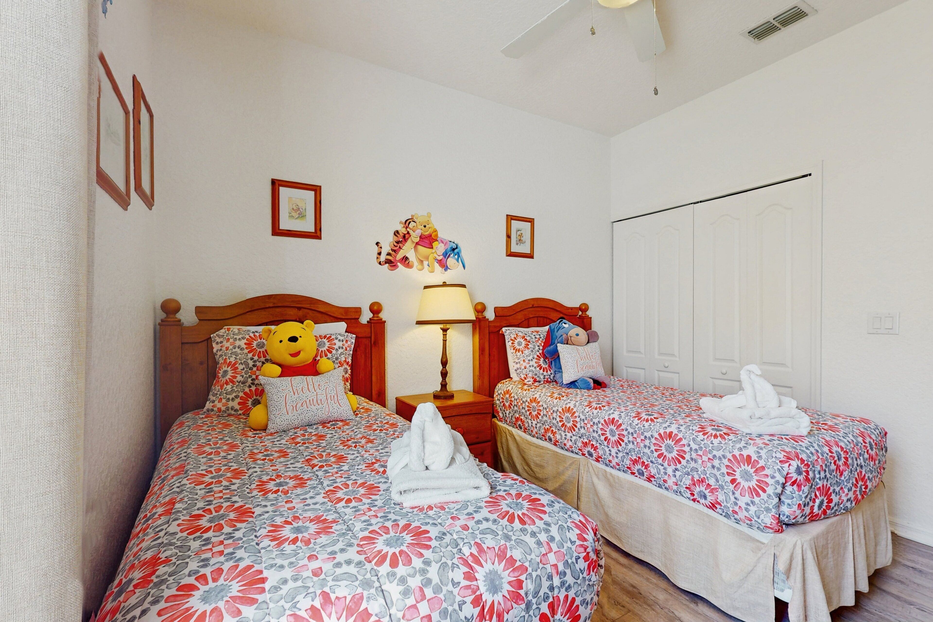 A hotel room with two beds, a nightstand, a lamp, and a wall with framed pictures.