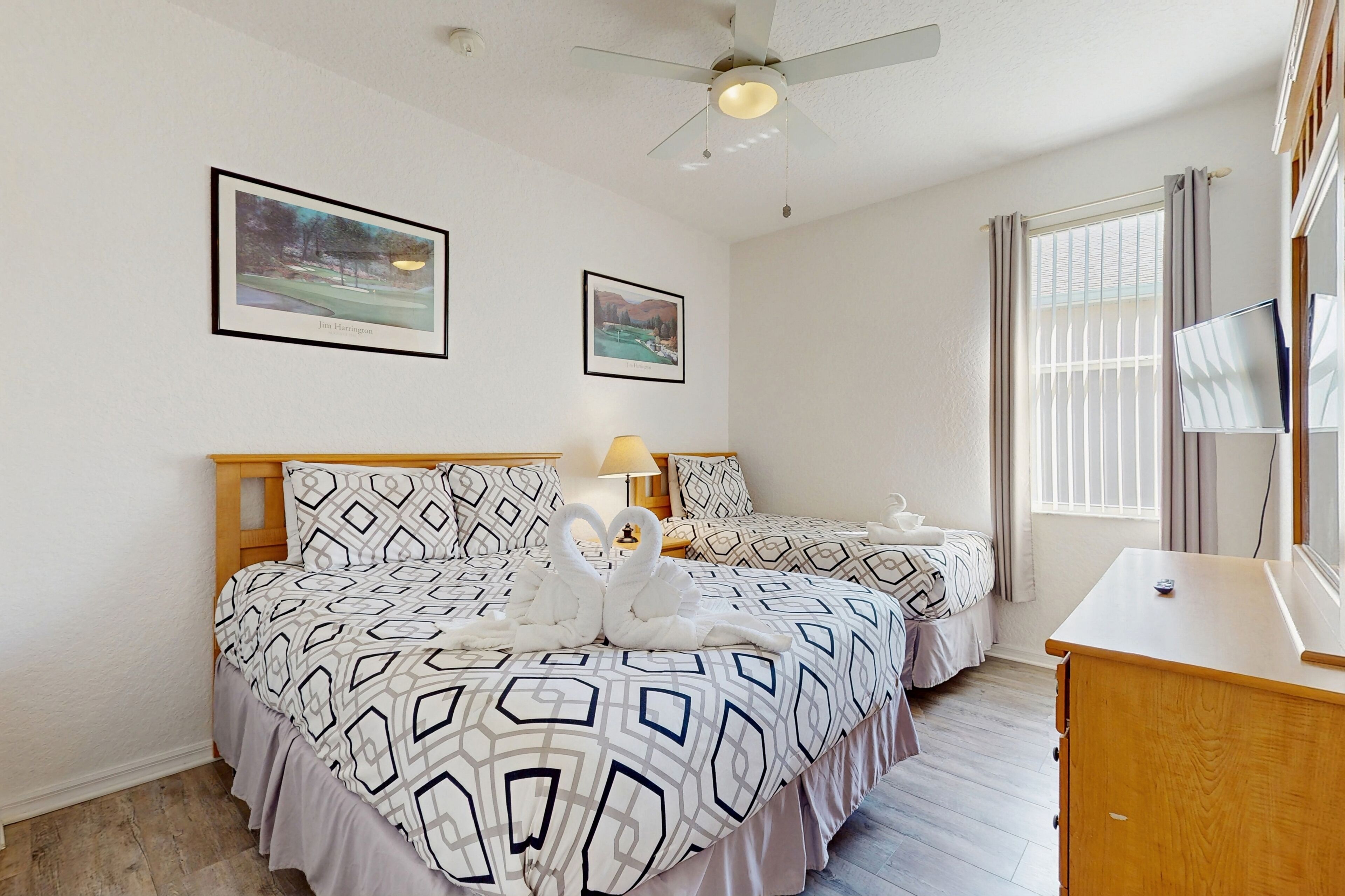 A hotel room with two beds, a ceiling fan, and artwork on the walls.