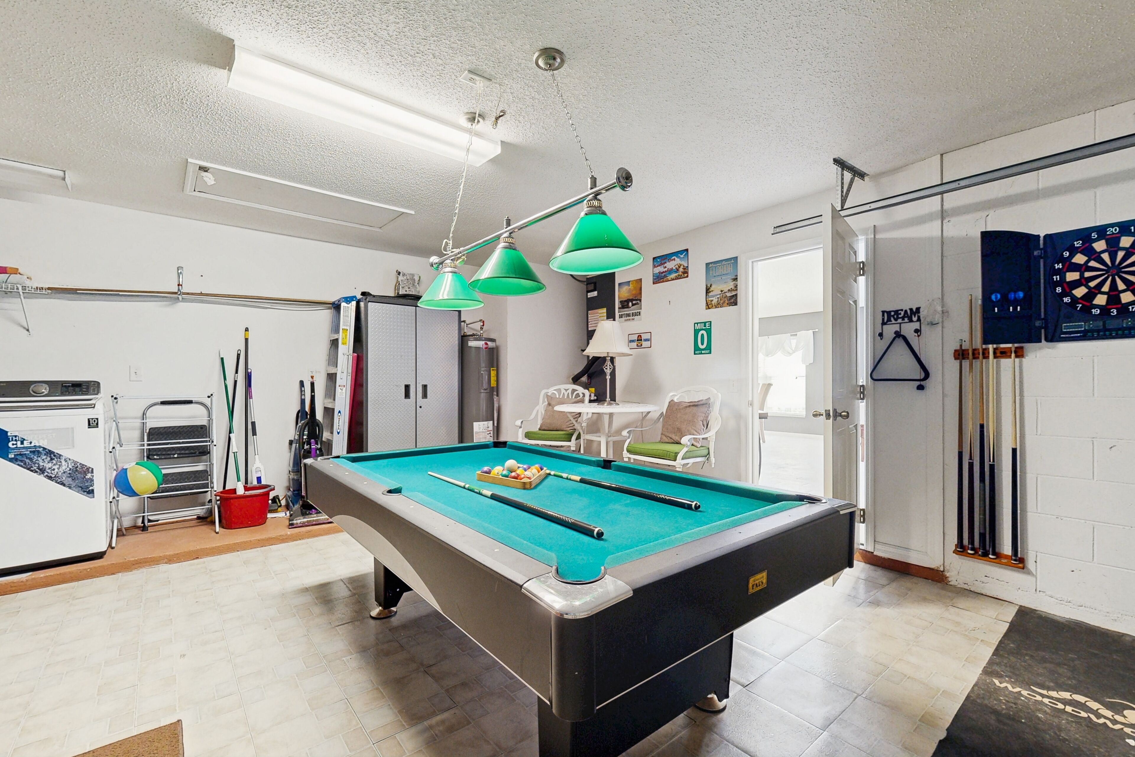 A pool table with green overhead lights, a dartboard, and a billiards rack.