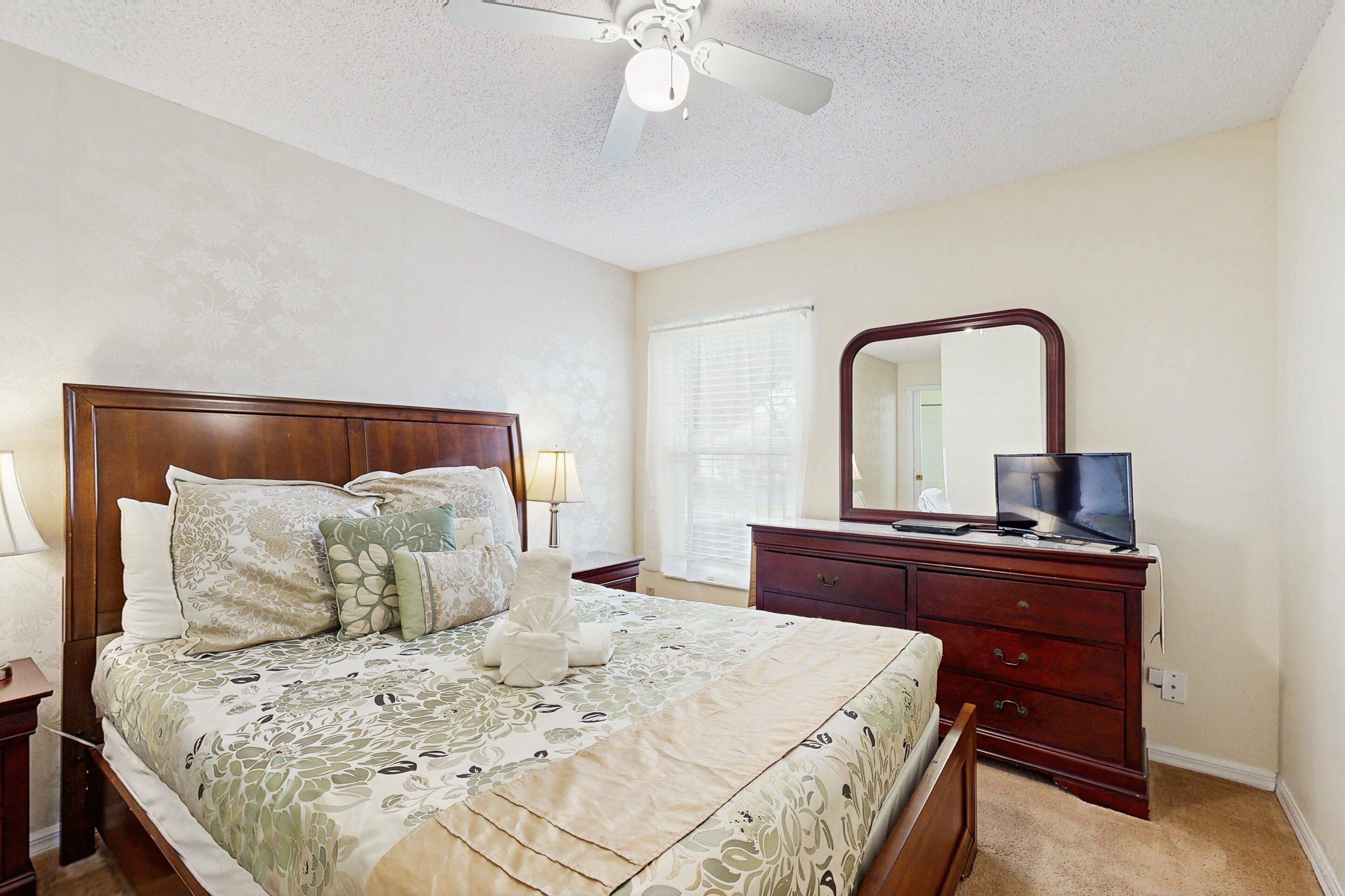 Une chambre à coucher comprenant un lit, une commode, un téléviseur et un ventilateur de plafond.