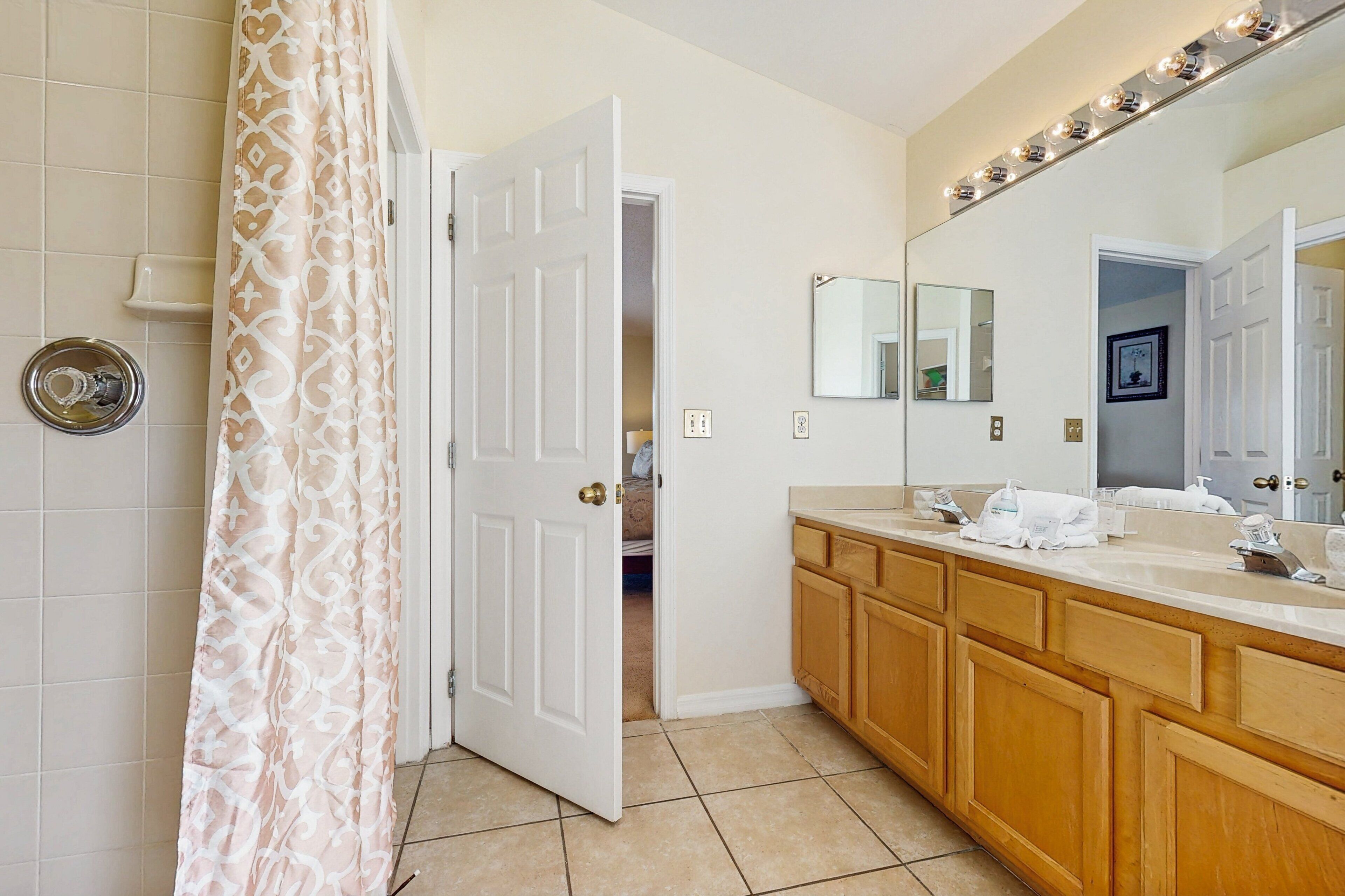 A bathroom with a shower curtain, a sink with a mirror, and a door leading to another room.