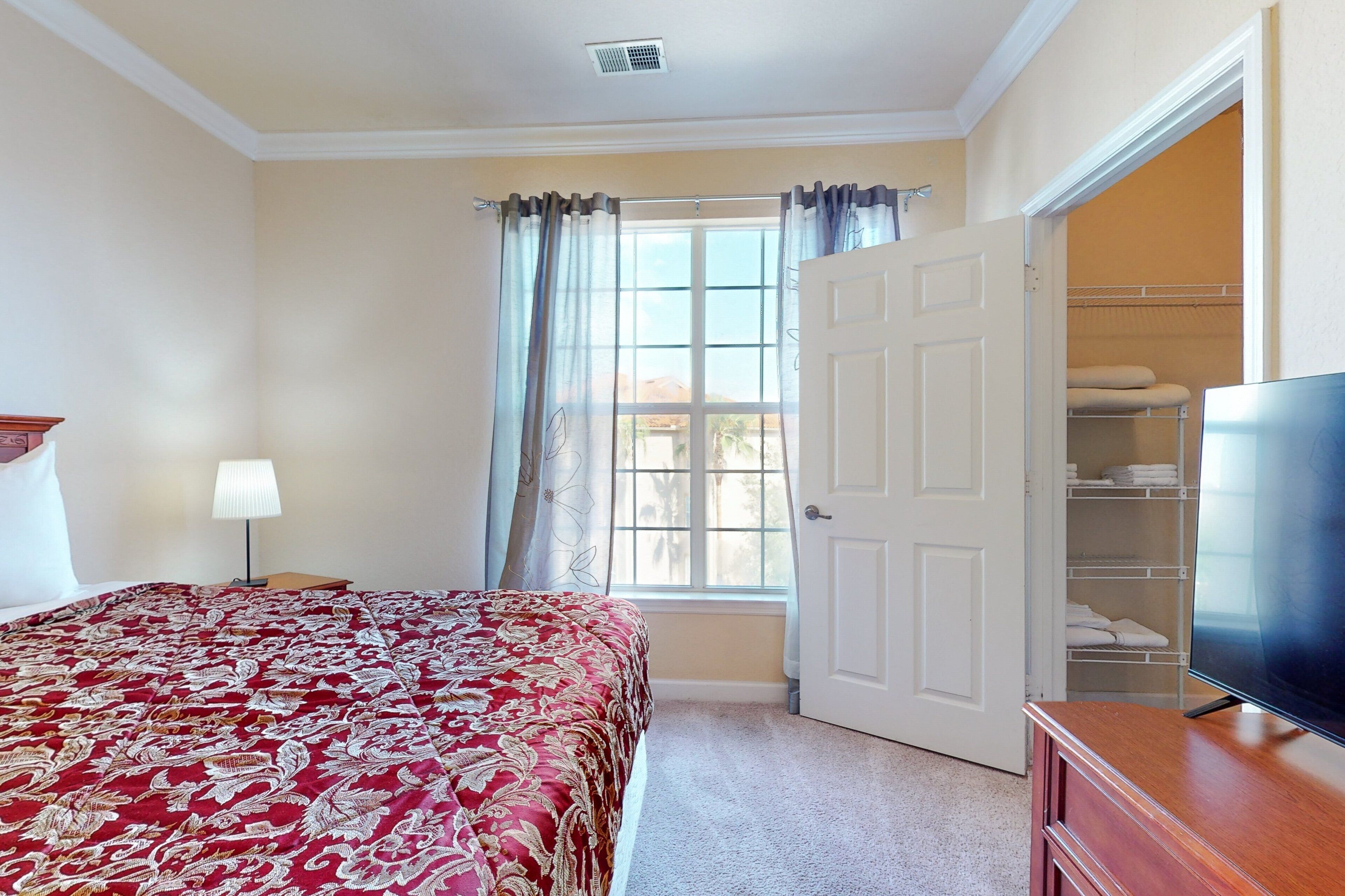Un dormitorio con cama, televisión, armario y ventana con cortinas.