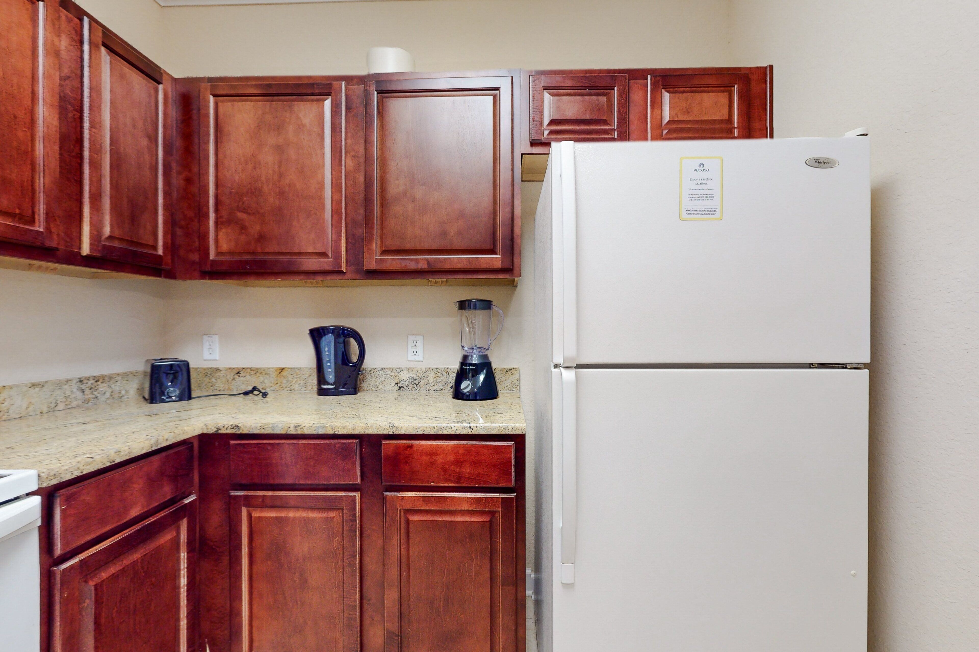 Una cocina con armarios de madera, un refrigerador blanco, una licuadora y una tostadora sobre la encimera.