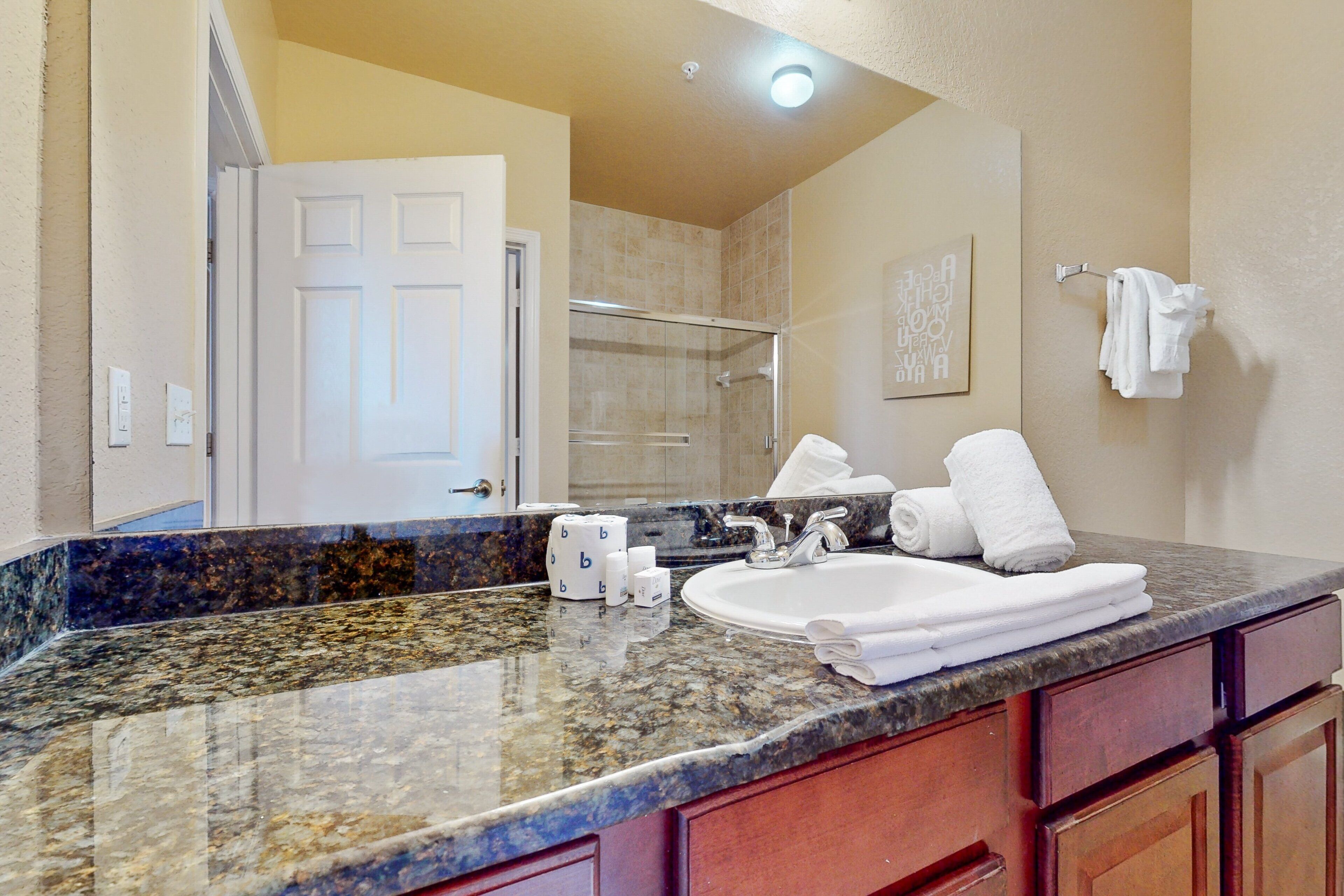 A bathroom with a granite countertop, a sink, a mirror, and a shower.