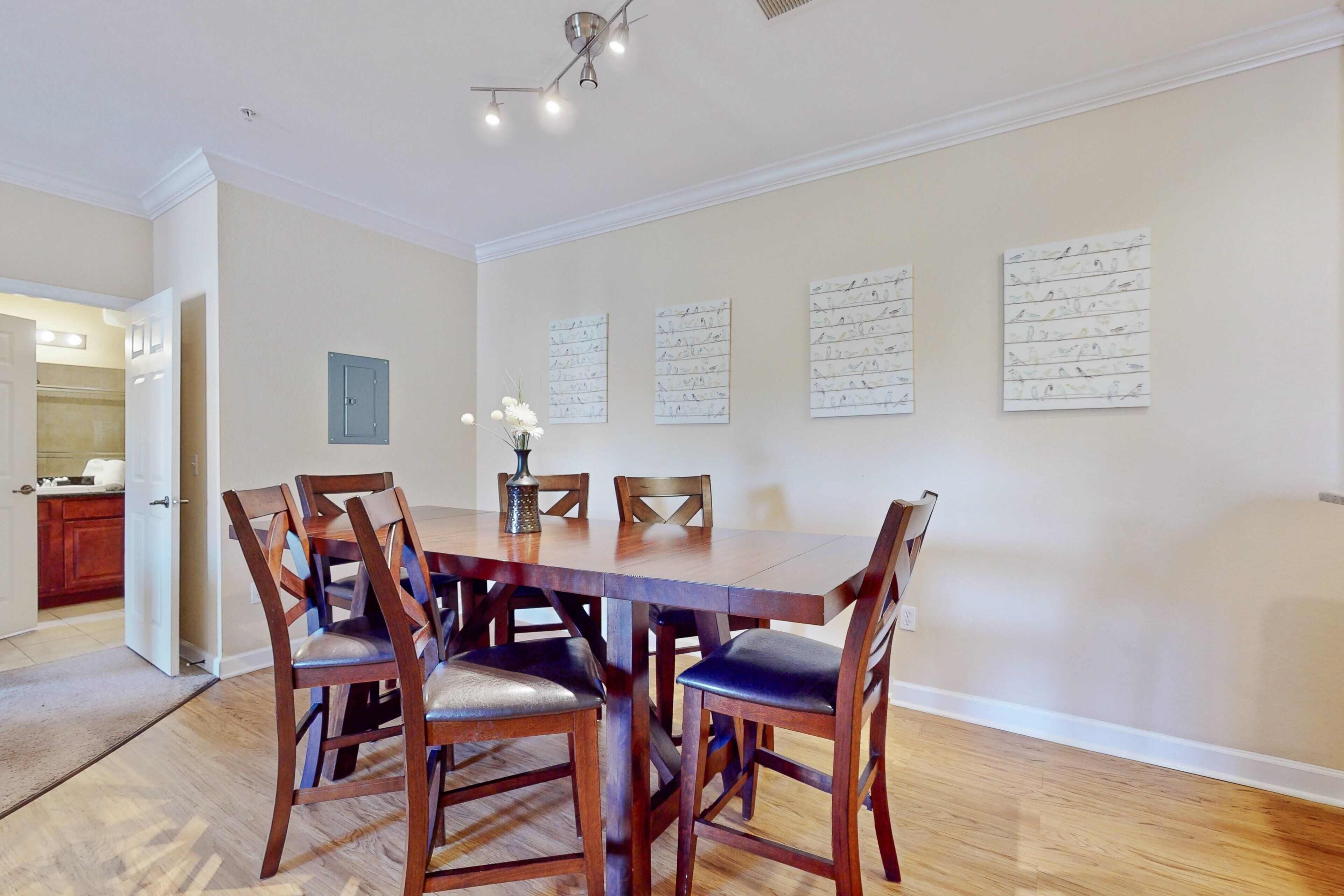 A dining area with a wooden table and chairs, a vase with flowers, and wall art.
