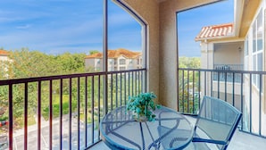 A balcony with a round table and chairs, a potted plant, and a view of houses and trees. - Tuscan Terrace (Davenport)