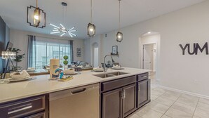 Una cocina moderna con una isla grande, iluminación colgante y un cartel que dice 'YUM'.