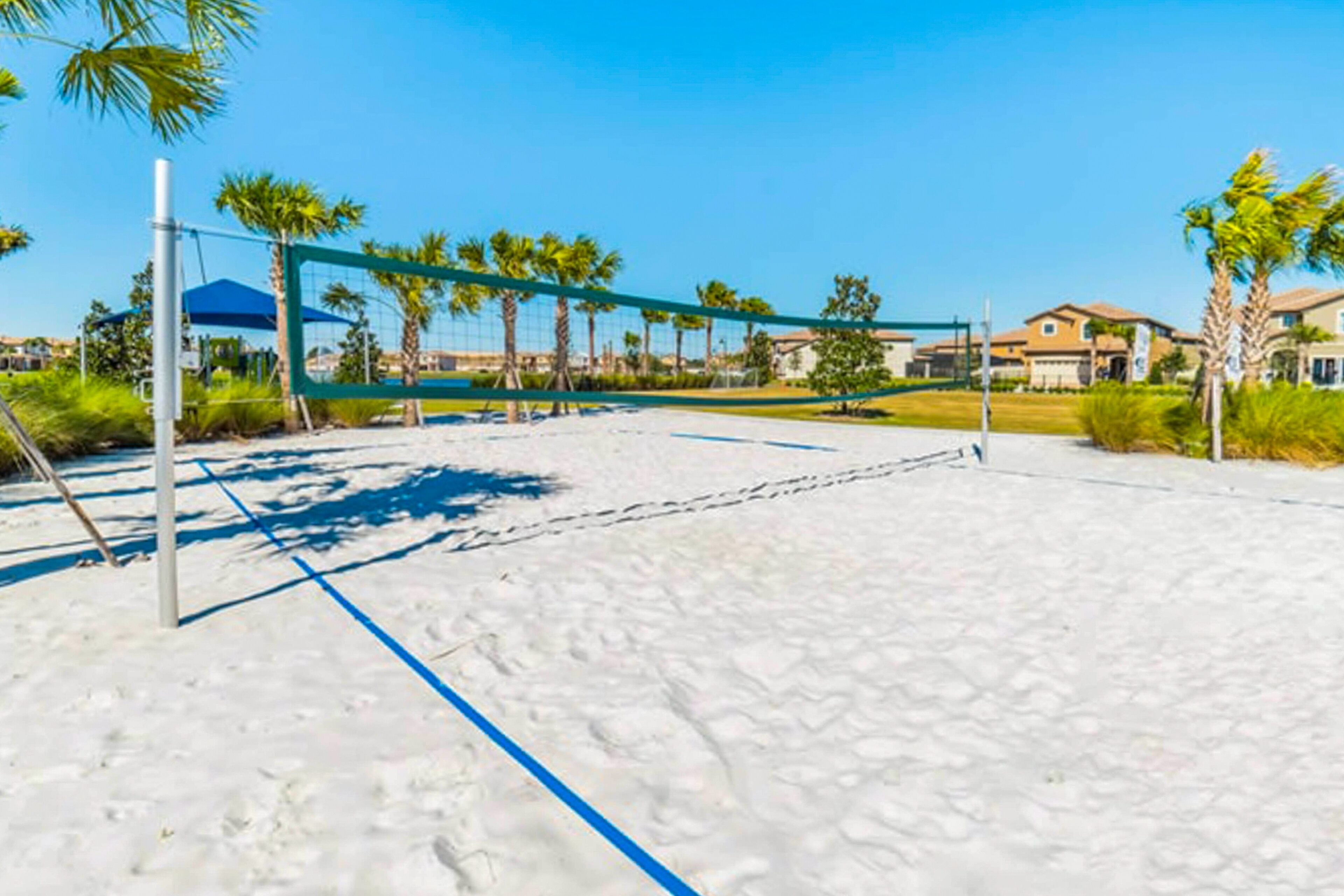 Un terrain de volley-ball de plage avec un filet, entouré de palmiers et avec des maisons en arrière-plan.