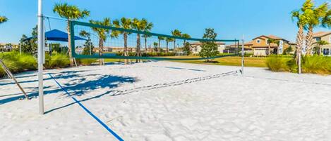Un terrain de volley-ball de plage avec un filet, entouré de palmiers et avec des maisons en arrière-plan.