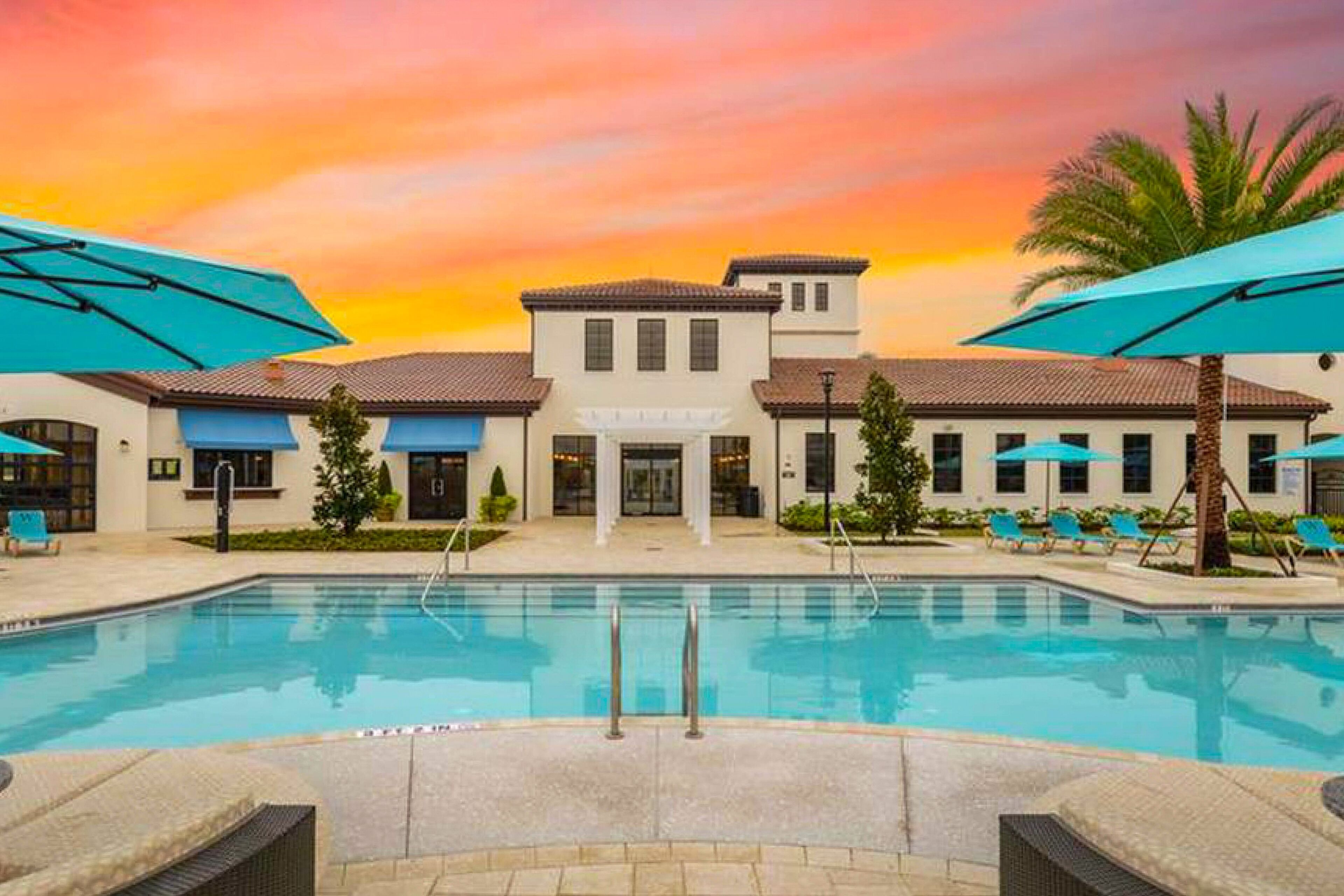A hotel with a pool, outdoor seating, and a sunset view.