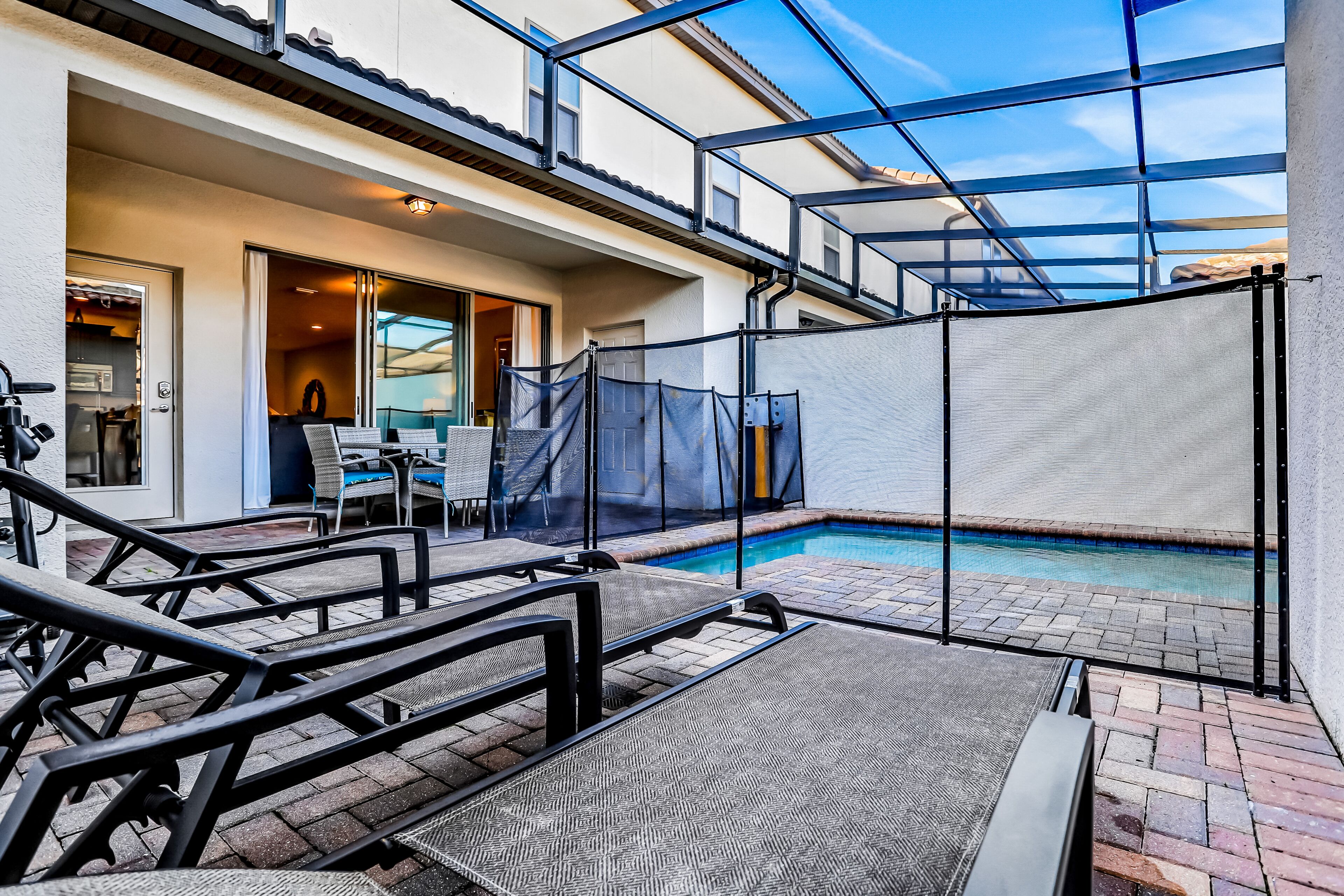 A pool area with a covered patio, outdoor seating, and a view of the pool through a glass enclosure.