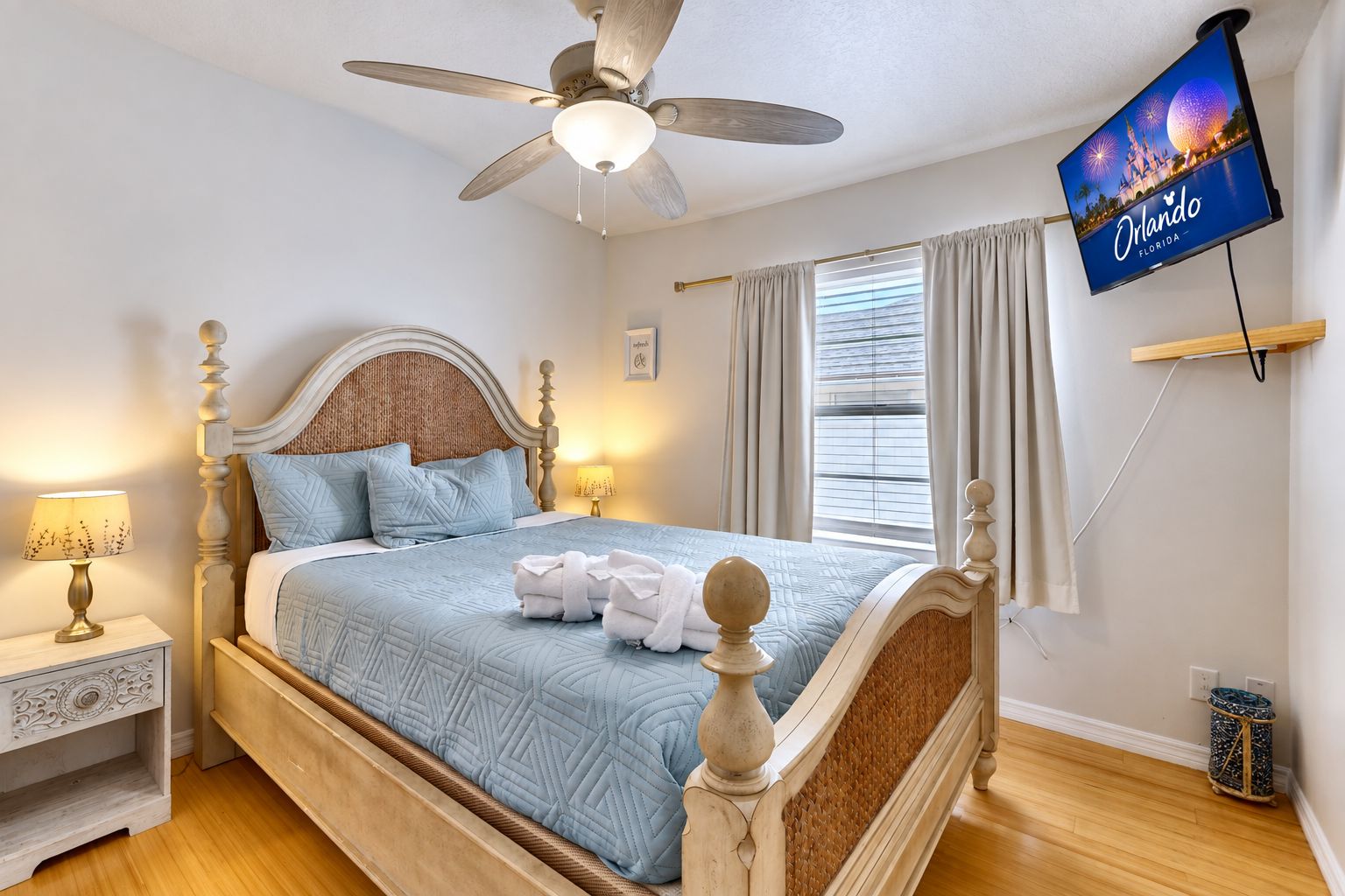 A hotel room with a bed, a ceiling fan, a television displaying Orlando, Florida, and a window with curtains.