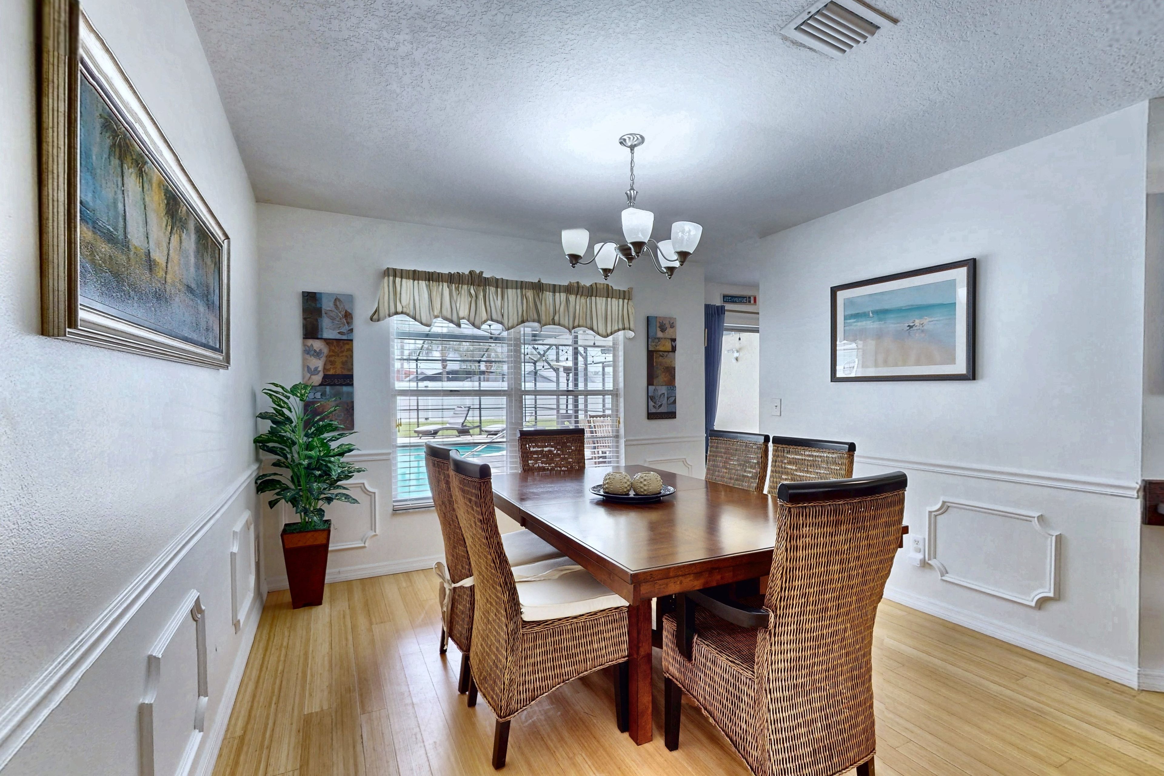 A dining area with a wooden table, wicker chairs, a potted plant, and artwork on the walls.