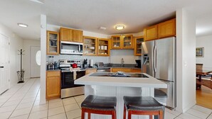 A modern kitchen with wooden cabinets, a stainless steel refrigerator, and a central island with stools. - Private Pool, Home Theater & Dog-friendly Retreat Near Disney (Kissimmee)