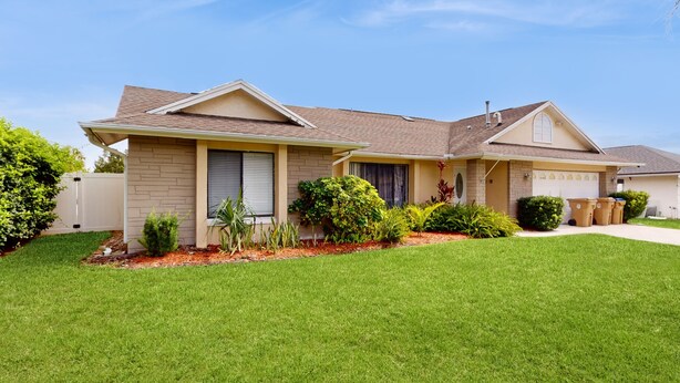 A two-story house with a well-maintained lawn, a garage, and a variety of shrubs and plants. - Private Pool, Home Theater & Dog-friendly Retreat Near Disney (Kissimmee)