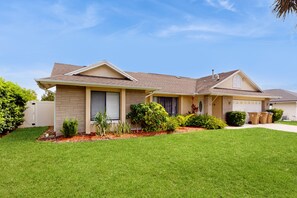 A two-story house with a well-maintained lawn, a garage, and a variety of shrubs and plants. - Private Pool, Home Theater & Dog-friendly Retreat Near Disney (Kissimmee)