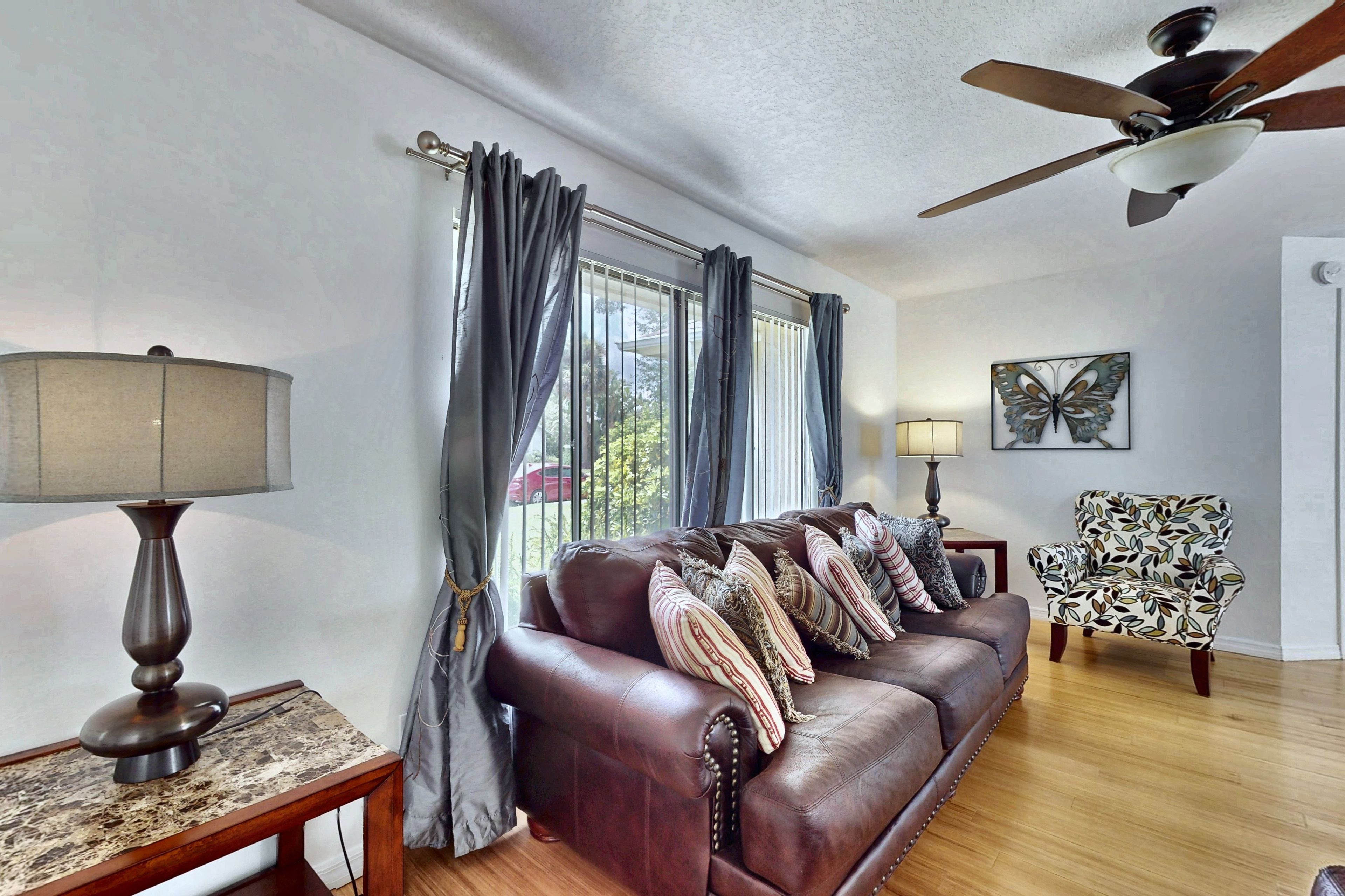 A living room with a leather sofa, two lamps, a butterfly wall art, and a ceiling fan.