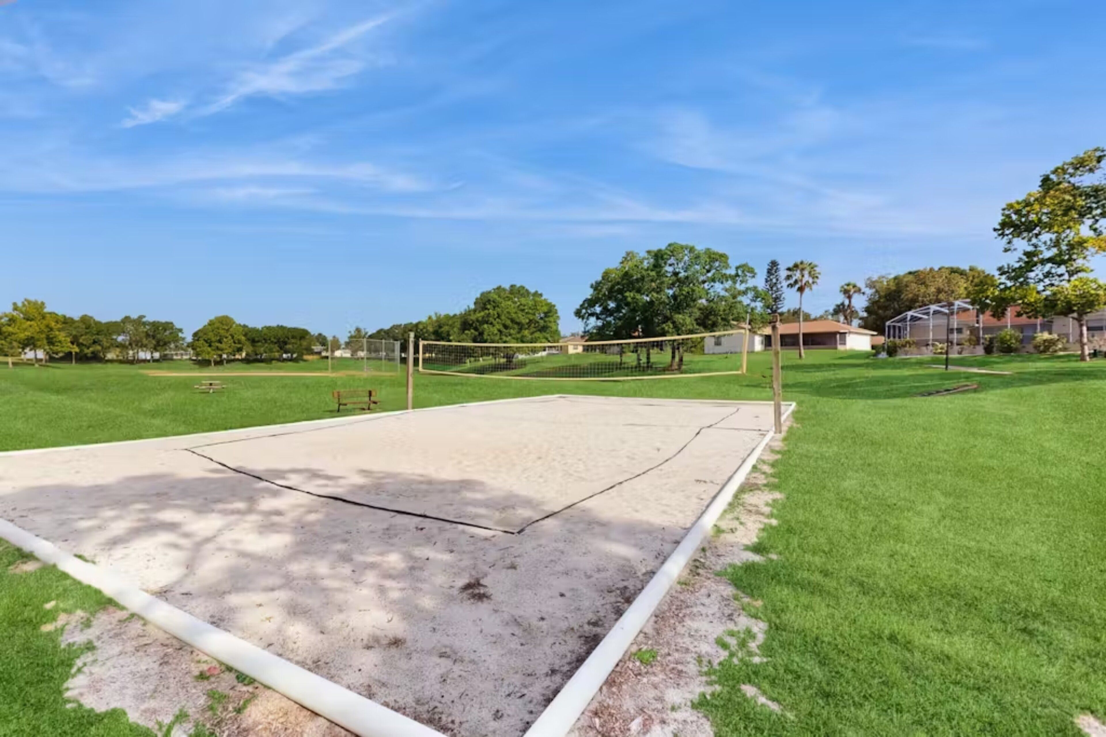 Una cancha de voleibol con red, rodeada de césped verde y árboles.
