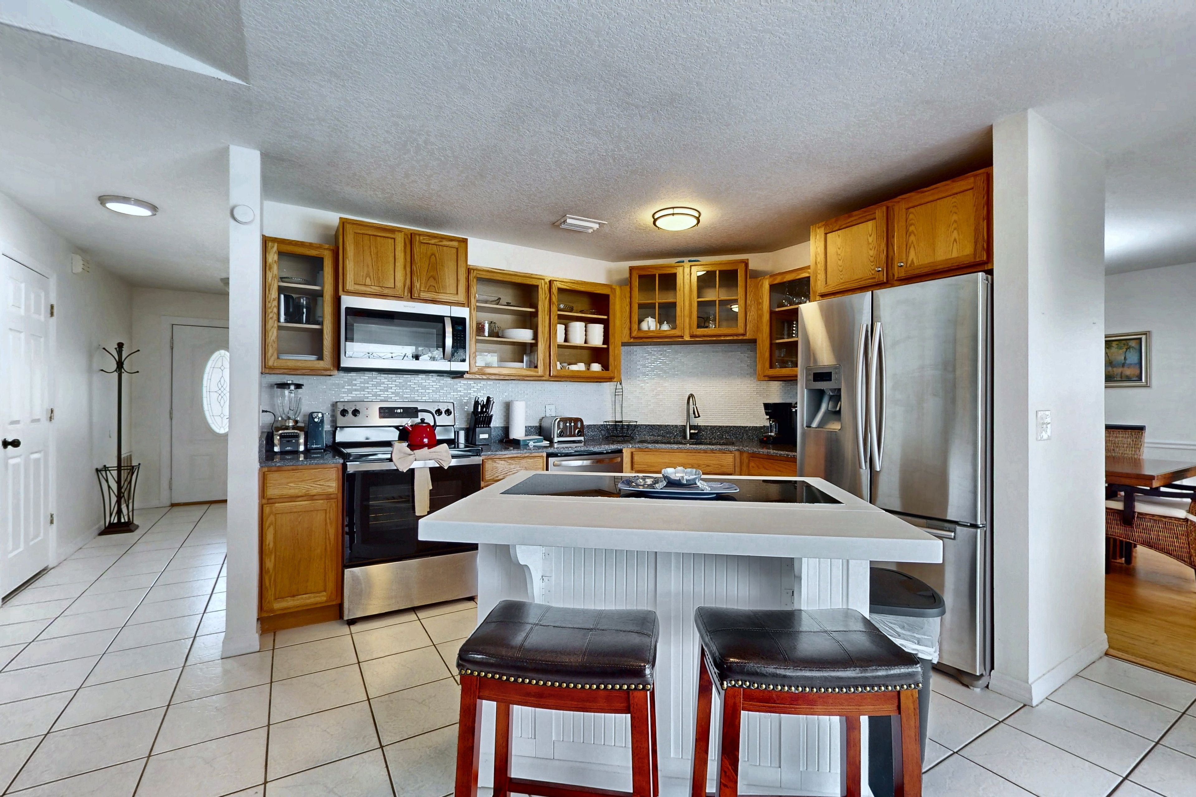 Una cocina con armarios de madera, un refrigerador de acero inoxidable, un microondas y una isla grande con taburetes.