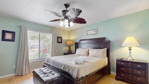 A bedroom with a bed, a ceiling fan, a nightstand, a lamp, a window with curtains, and a wall-mounted picture. - Private Pool, Home Theater & Dog-friendly Retreat Near Disney (Kissimmee)