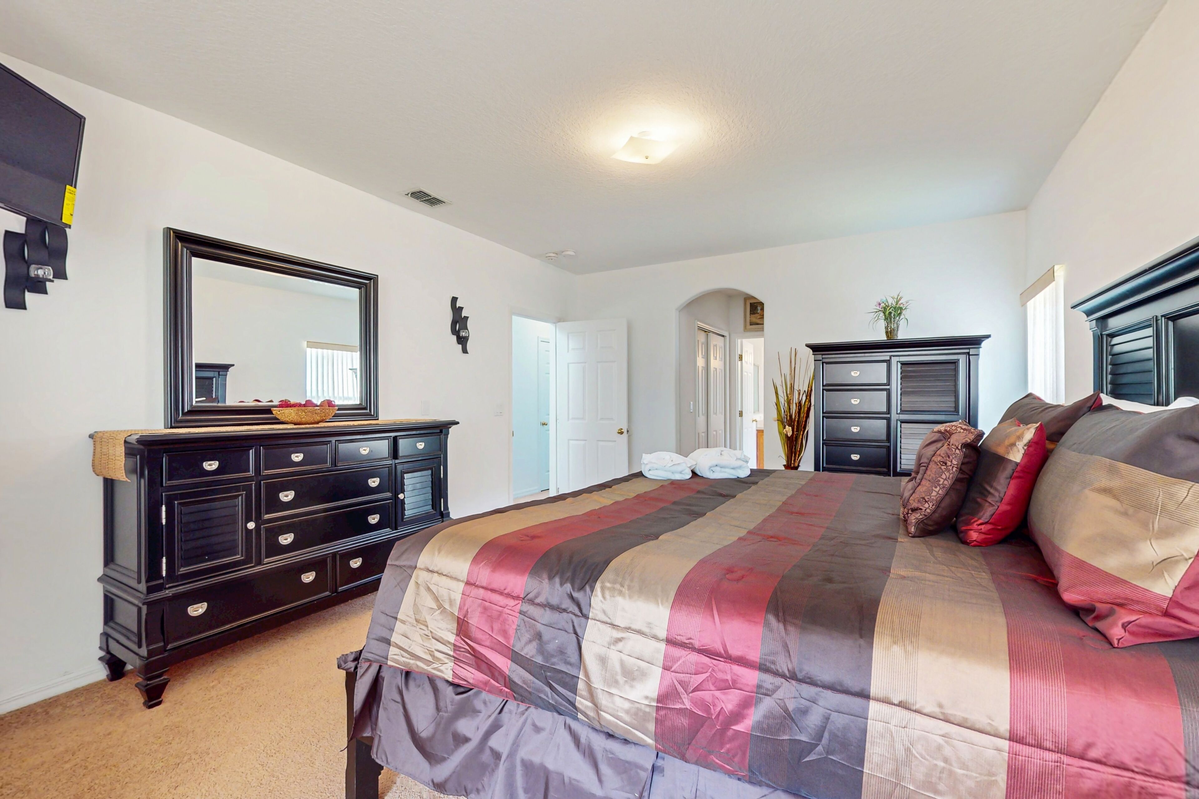 Een slaapkamer met een groot bed, een dressoir, een spiegel en een deur naar een andere kamer.