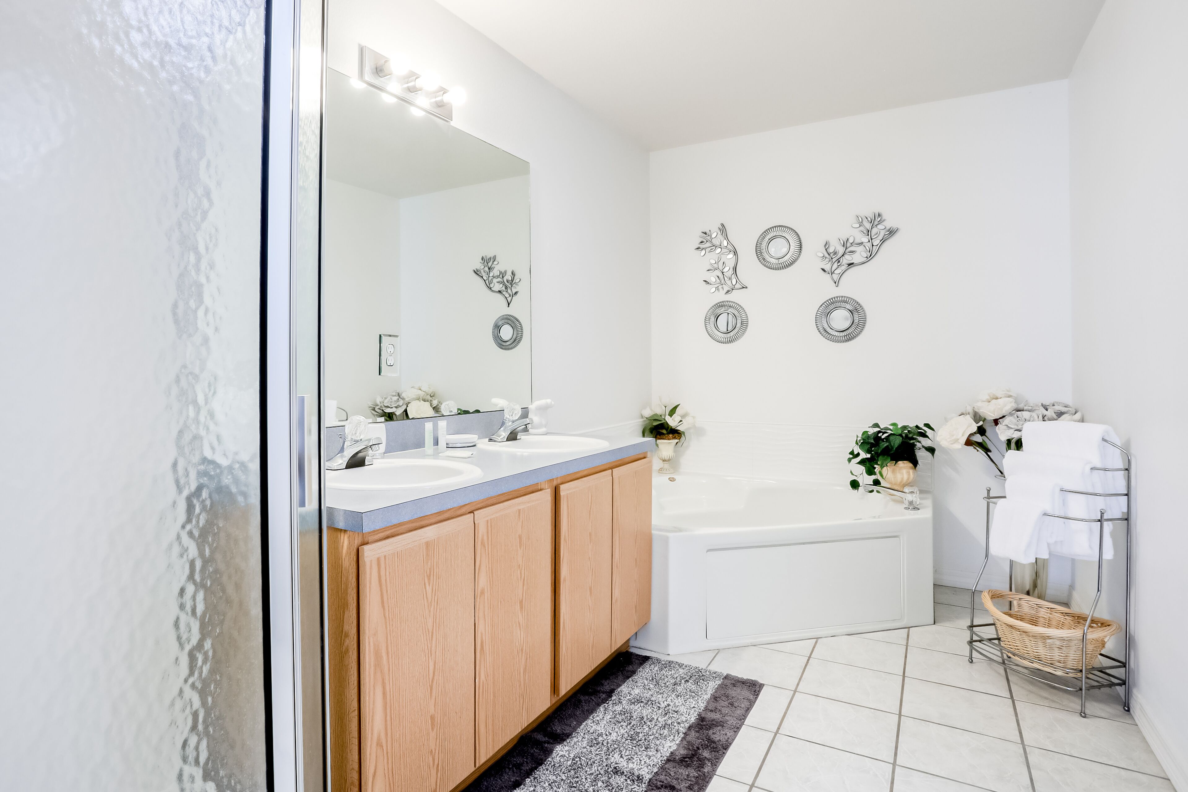 A modern bathroom with two sinks, a large mirror, a bathtub, and decorative wall art.