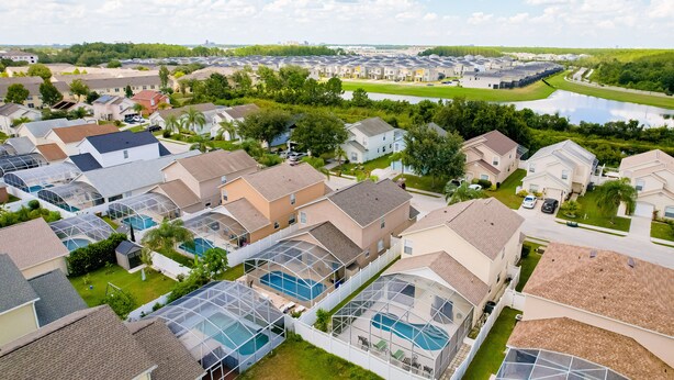 A residential area with houses, a swimming pool, and a large building complex in the background. - Enchanting Dog-friendly Home With Pool, Lanai, Central AC, & Washer/dryer (Kissimmee)