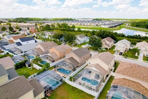 A residential area with houses, a swimming pool, and a large building complex in the background. - Enchanting Dog-friendly Home With Pool, Lanai, Central AC, & Washer/dryer (Kissimmee)